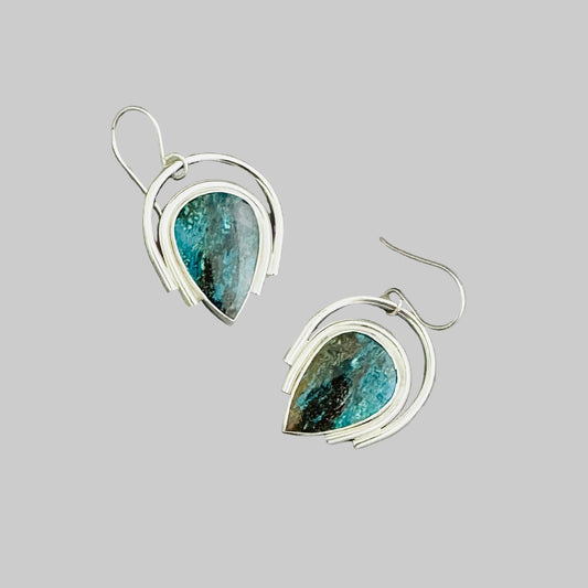 A pair of silver dangle earrings with reverse teardrop-shaped turquoise-blue and brown stone inlays, displayed on a neutral light gray background.
